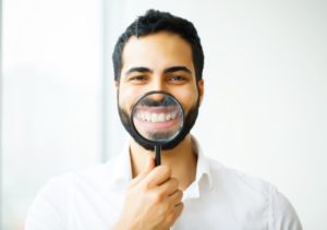 man holding magnifying glass to his smile with porcelain veneers in West Bloomfield 